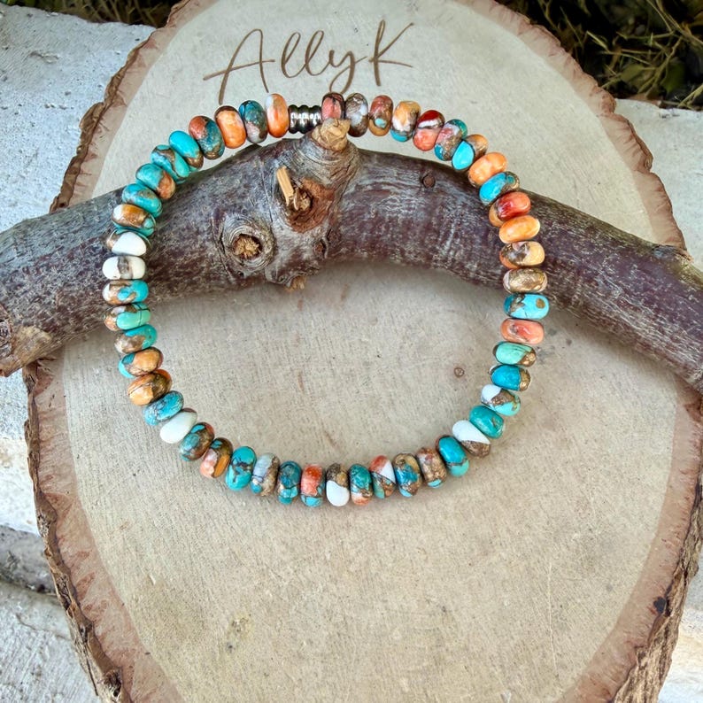 May include: A circular beaded bracelet featuring small, flat, round beads in a variegated mix of turquoise, orange, white, and brown colors. The bracelet includes a single metallic silver-toned spacer bead and is arranged in a continuous loop.
