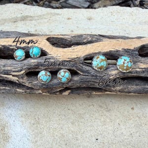 May include: Turquoise and brown stone stud earrings in 4mm, 5mm, and 6mm sizes. The earrings are set in silver-colored metal and displayed on a piece of driftwood. The text "4mm", "5mm", and "6mm" is written on the wood.