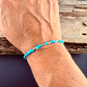 May include: A delicate bracelet featuring small, irregular, bright turquoise-colored beads interspersed with thin, cylindrical silver-toned metal spacers, arranged in a single strand that encircles the wrist.