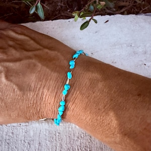 May include: A bracelet featuring small, irregular, bright turquoise-colored stone chips interspersed with thin, metallic silver-toned cylindrical beads. The stones are vibrant blue and have a polished, tumbled appearance, creating a continuous beaded strand.