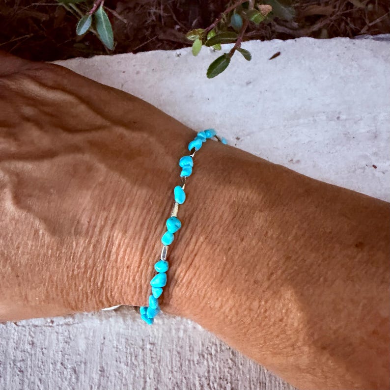 May include: A bracelet featuring small, irregular, bright turquoise-colored stone chips interspersed with thin, metallic silver-toned cylindrical beads. The stones are vibrant blue and have a polished, tumbled appearance, creating a continuous beaded strand.