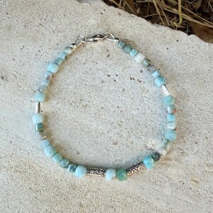 Puede incluir: Una pulsera de cuentas con peque&ntilde;as piedras de corte cuadrado en azul claro y verde p&aacute;lido, intercaladas con espaciadores cil&iacute;ndricos de tono plateado. La pulsera se asegura con un cierre de mosquet&oacute;n plateado y una peque&ntilde;a argolla.