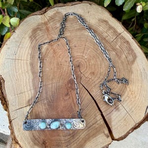 May include: A sterling silver necklace featuring a rectangular bar pendant with a textured, oxidized finish and three small, round, light blue cabochon stones. The pendant is attached to a sturdy, dark silver-toned link chain with a lobster clasp.