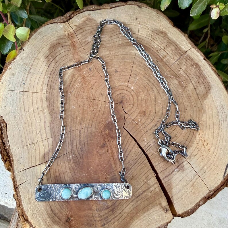 May include: A sterling silver necklace featuring a rectangular bar pendant with a textured, oxidized finish and three small, round, light blue cabochon stones. The pendant is attached to a sturdy, dark silver-toned link chain with a lobster clasp.