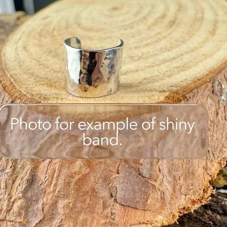 May include: A silver-colored, hammered metal band ring. The ring is wide and has a textured surface. The image includes the text "Photo for example of shiny band."