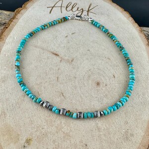 May include: Turquoise beaded anklet with silver accents. The anklet features small, round turquoise beads strung together, interspersed with silver-colored, ridged beads. The clasp is silver. The anklet is displayed on a wooden surface with the name "Allyk" written on it.