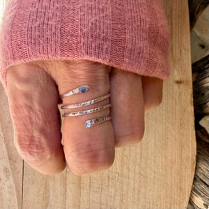 May include: A silver-toned metal ring featuring a spiral wrap design that encircles the finger multiple times. The band has a hammered, textured finish with rounded, polished ends, creating a continuous coil appearance around the finger.
