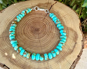 May include: A beaded necklace featuring round, turquoise-colored stones with brown matrix patterns. The beads are strung together with small silver-toned spacers and secured with a silver-toned lobster claw clasp at the top of the circular arrangement.