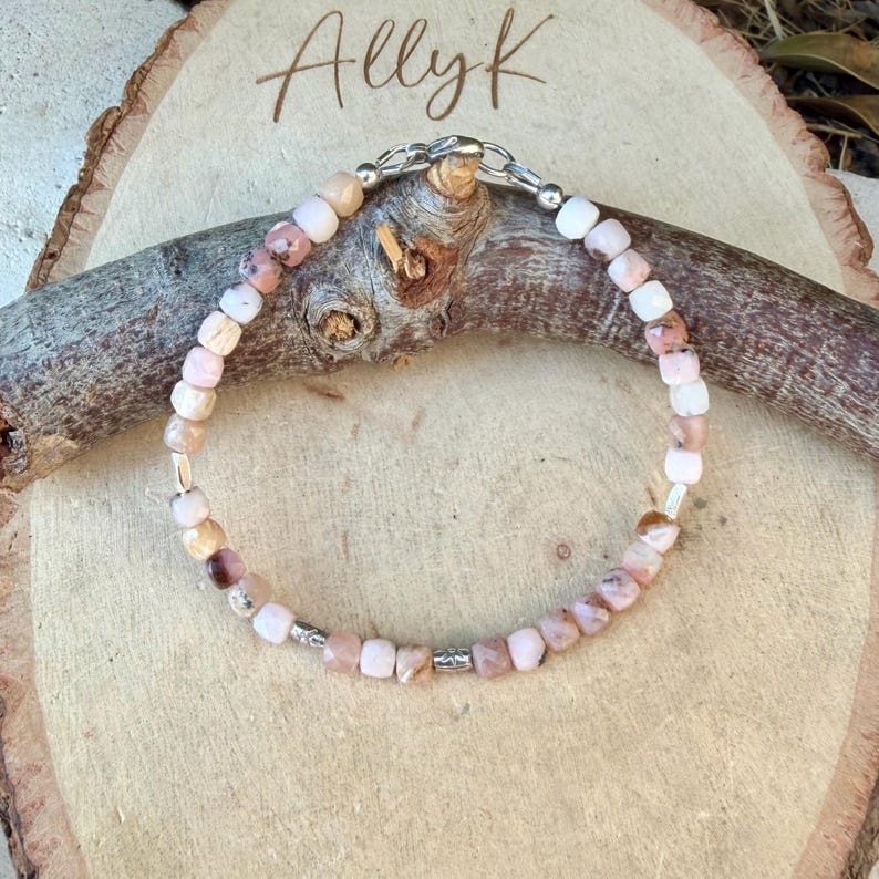 May include: A beaded bracelet featuring small, faceted, light pink and white stone beads arranged in a circular pattern. The bracelet includes metallic silver-toned spacer beads and a silver-toned lobster claw clasp closure for secure fastening.