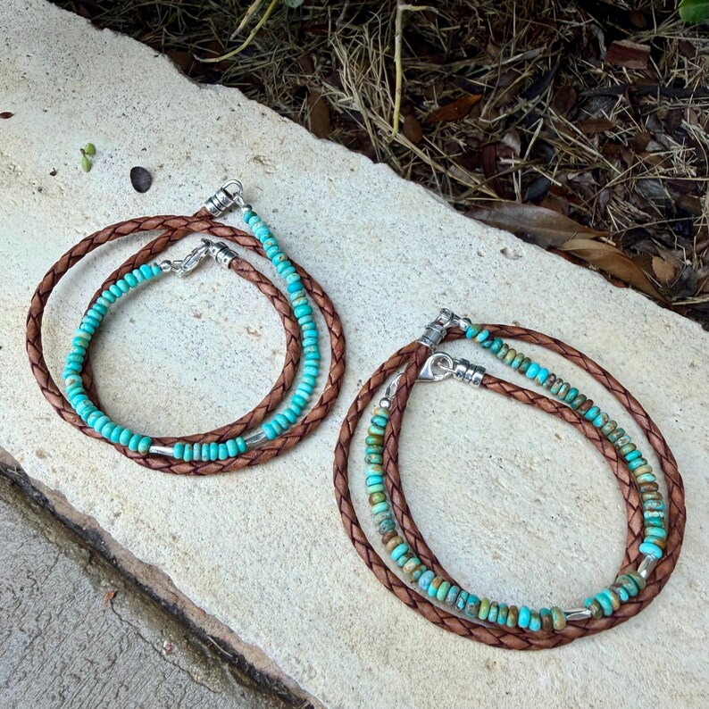 May include: Two wrap bracelets featuring braided brown leather cords paired with strands of small turquoise beads. Each bracelet includes silver-toned metal clasps and accents, showcasing a combination of smooth and variegated blue-green stone beads.