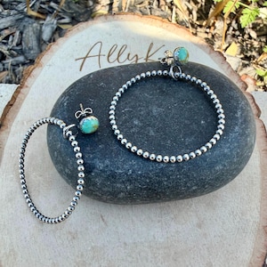 Puede incluir: Pendientes de aro y un pendiente de bot&oacute;n de plata con piedras de color turquesa. Los pendientes se exhiben sobre una piedra gris oscura y una superficie de madera. La palabra "Ally K" est&aacute; escrita en cursiva sobre la madera.