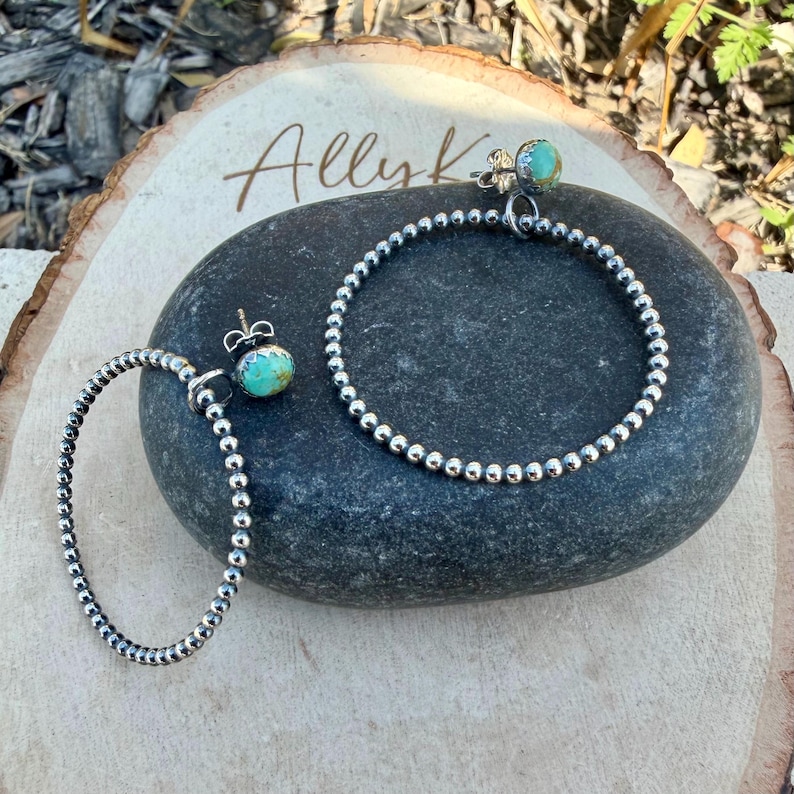 Puede incluir: Pendientes de aro y un pendiente de bot&oacute;n de plata con piedras de color turquesa. Los pendientes se exhiben sobre una piedra gris oscura y una superficie de madera. La palabra "Ally K" est&aacute; escrita en cursiva sobre la madera.