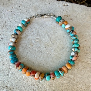Pode incluir: Uma pulseira de contas com pedras redondas e polidas em tons de turquesa, laranja, branco e castanho. As contas est&atilde;o enfiadas e presas com um fecho de mosquet&atilde;o de metal prateado, criando uma disposi&ccedil;&atilde;o circular de pedras naturais coloridas.