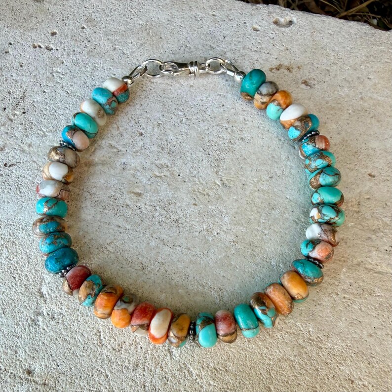 Pode incluir: Uma pulseira de contas com pedras redondas e polidas em tons de turquesa, laranja, branco e castanho. As contas est&atilde;o enfiadas e presas com um fecho de mosquet&atilde;o de metal prateado, criando uma disposi&ccedil;&atilde;o circular de pedras naturais coloridas.