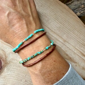 May include: A multi-strand bracelet set featuring two thin brown leather cords and two strands of small, round, turquoise-colored beads. The turquoise beads are interspersed with tiny silver-toned metal spacers, creating a layered look.