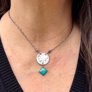 Op de afbeelding: Zilveren ketting met een muntvormige hanger met een Indiaans profiel en een turkoois edelsteen. De ketting heeft een ketting met kleine turkoois kralen en een vierkante turkoois steen.