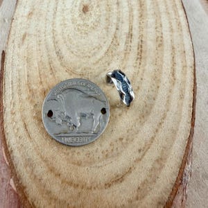 May include: A silver-toned ring with a textured design sits next to a silver buffalo nickel. The coin is stamped with the words "United States of America" and "Five Cents". The ring has a unique, organic shape.