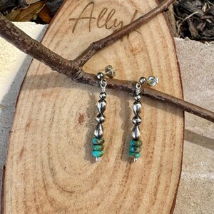 May include: Silver dangle earrings with turquoise and silver beads. The earrings have a post backing and are displayed on a wooden surface with a branch. The word "Ally" is written on the wood.