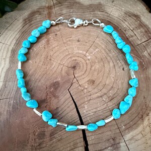 May include: A bracelet featuring small, irregular, bright blue turquoise-colored stones interspersed with smooth, cylindrical silver-toned metal beads. The piece is secured with a silver-toned lobster claw clasp.