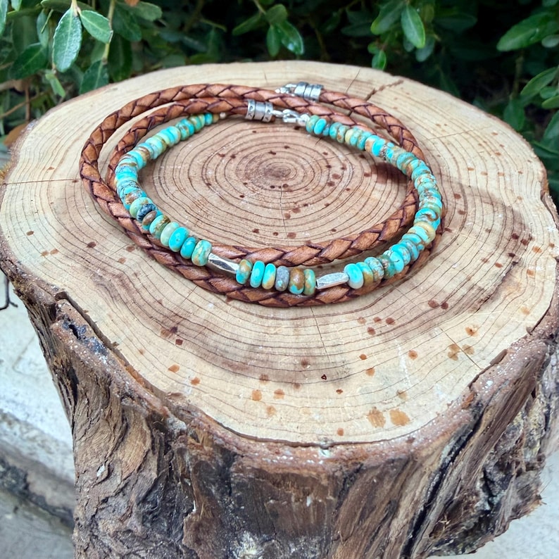 May include: A wrap bracelet featuring a braided brown leather cord and a strand of round turquoise beads. The design includes small silver-toned metal spacers interspersed among the beads and a silver-toned metal clasp closure at the ends.