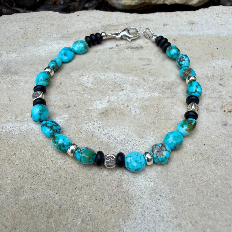 May include: Turquoise beaded bracelet with silver accents and a secure clasp. The bracelet features round, light blue turquoise beads interspersed with silver-colored beads and black beads. A stylish accessory.