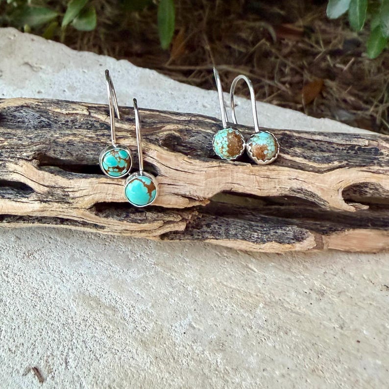 May include: Two pairs of drop earrings featuring round turquoise stones with brown matrix patterns set in silver-toned metal. Each earring has a curved wire hook for attachment, showcasing a polished finish on the stones and a simple metal setting.