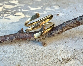 May include: A gold-toned metal ring with a bypass spiral design. The band features a hammered, textured finish on the outer surface, creating a reflective appearance. The ring is open-ended, with two tapered ends that overlap slightly in a coil shape.