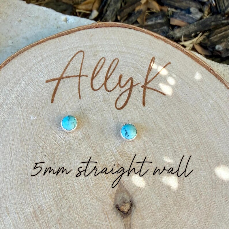 May include: A pair of turquoise stud earrings with a silver bezel, displayed on a wooden surface. The earrings are 5mm in size and are labeled "Allyk" and "5mm straight wall" in brown script.