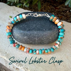 May include: A beaded bracelet featuring round, multi-colored stone beads in shades of turquoise, orange, and white, accented with small dark metal spacers. The bracelet is secured with a silver-toned metal swivel lobster clasp closure.