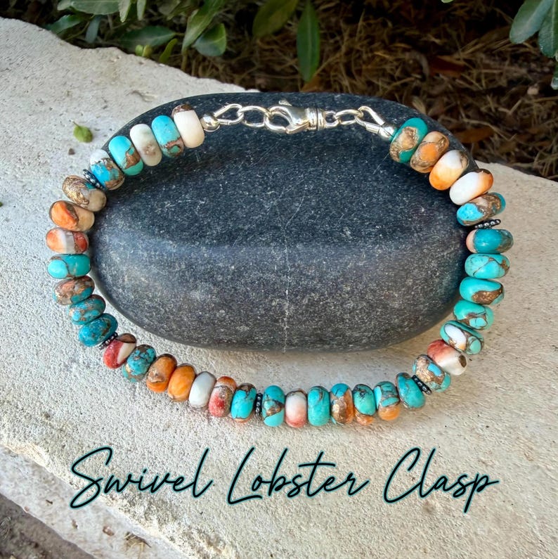 May include: A beaded bracelet featuring round, multi-colored stone beads in shades of turquoise, orange, and white, accented with small dark metal spacers. The bracelet is secured with a silver-toned metal swivel lobster clasp closure.