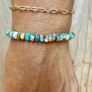 May include: A gold-toned chain bracelet with textured oval links paired with a beaded bracelet featuring round, multi-colored turquoise and copper-colored stones in shades of blue, white, and orange, arranged in a repeating pattern.