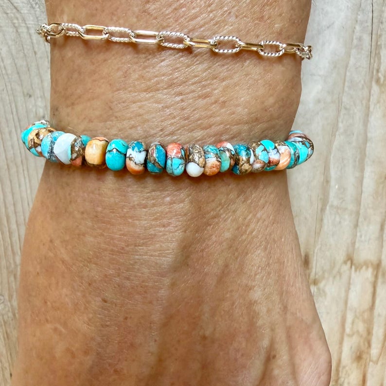 May include: A gold-toned chain bracelet with textured oval links paired with a beaded bracelet featuring round, multi-colored turquoise and copper-colored stones in shades of blue, white, and orange, arranged in a repeating pattern.