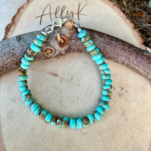 May include: A beaded bracelet featuring round, disc-shaped turquoise stones with natural brown matrix inclusions. The beads are strung together with small silver-toned metal spacers and secured with a silver-toned lobster claw clasp closure.