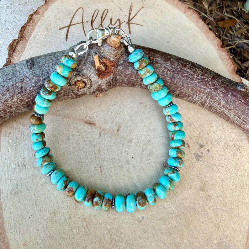 May include: A beaded bracelet featuring round, disc-shaped turquoise stones with natural brown matrix inclusions. The beads are strung together with small silver-toned metal spacers and secured with a silver-toned lobster claw clasp closure.
