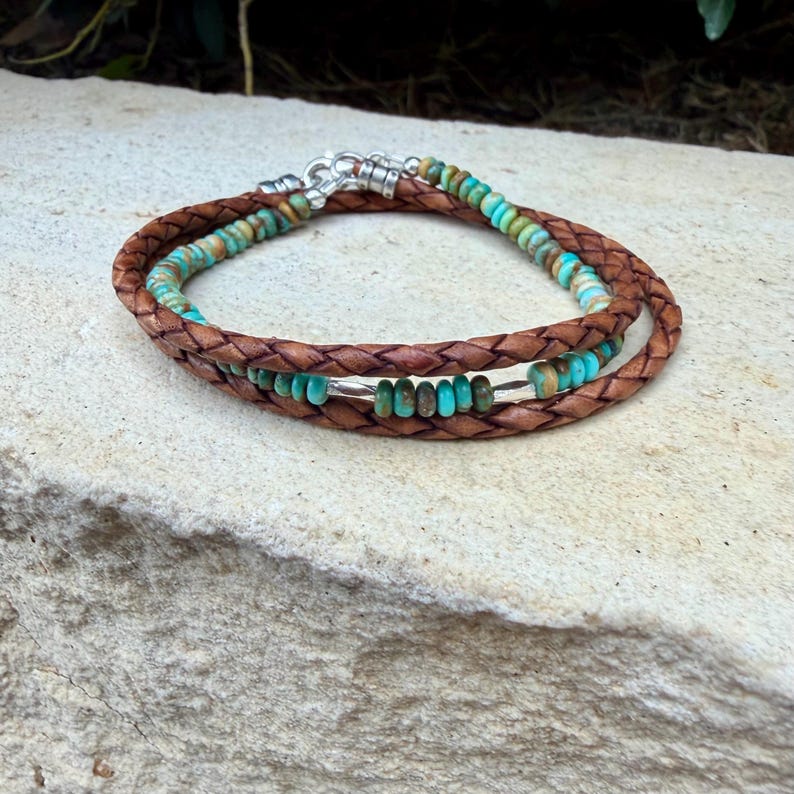 May include: A multi-strand wrap bracelet featuring braided brown leather cords interspersed with small, round, turquoise-colored stone beads and polished silver-toned metal accents, secured with a silver-toned metal clasp mechanism.