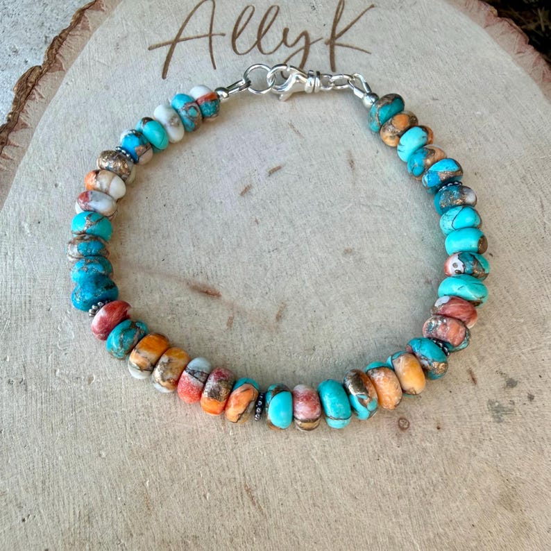 Pode incluir: Uma pulseira de contas com pedras redondas e achatadas em tons de turquesa, laranja e branco com veios naturais. A pulseira &eacute; fixada com um fecho lagosta e um anel de metal prateado. As contas est&atilde;o dispostas em formato circular.