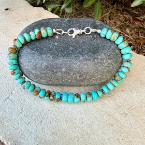 May include: A beaded bracelet featuring round, turquoise-colored stones with brown matrix inclusions. The beads are strung in a circular pattern and secured with a silver-toned metal lobster claw clasp, creating a continuous loop of natural-looking stones.