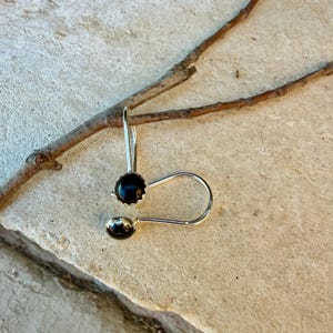 May include: A pair of silver earrings featuring round, faceted black stones set in a scalloped metal bezel. The earrings have a curved, open-loop wire design that hooks through the ear, showcasing a polished metallic finish and dark gems.