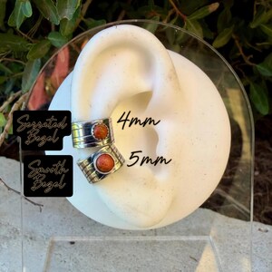 May include: Two silver ear cuffs featuring round orange stones. The top cuff has a serrated bezel and is 4mm wide, while the bottom cuff has a smooth bezel and is 5mm wide. Text on the image reads Serrated Bezel, Smooth Bezel, 4mm, and 5mm.