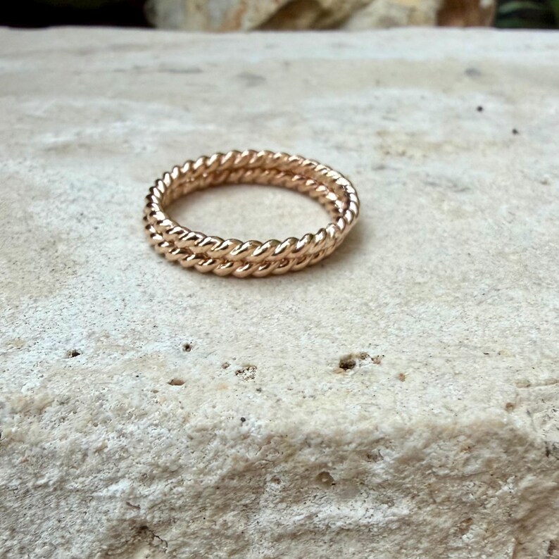 May include: A gold-colored ring with a twisted rope design. The ring features two bands of twisted metal, creating a textured and detailed appearance. The ring is set against a neutral background.