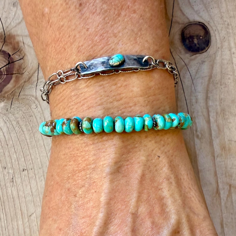 May include: A two-piece bracelet set featuring a silver-toned chain bracelet with a central hammered metal bar and a small turquoise stone, paired with a second bracelet composed of round, vibrant turquoise beads with brown matrix inclusions.