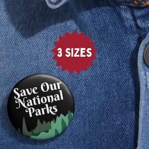 May include: A black button with the text "Save Our National Parks" and a green and white forest design. A red starburst shape with the text "3 SIZES" is also visible. The buttons are on a blue denim background.