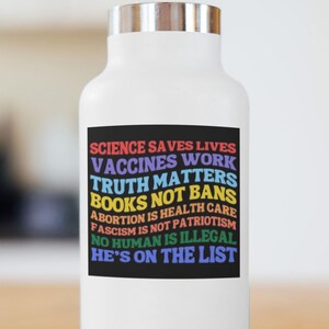 Pode incluir: Garrafa de &aacute;gua branca com tampa prateada. Um ret&acirc;ngulo preto na garrafa exibe texto colorido: "SCIENCE SAVES LIVES, VACCINES WORK, TRUTH MATTERS, BOOKS NOT BANS, ABORTION IS HEALTH CARE, FASCISM IS NOT PATRIOTISM, NO HUMAN IS ILLEGAL, HE'S ON THE LIST."
