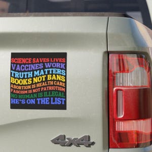 Pode incluir: Um autocolante retangular num ve&iacute;culo com o texto "SCIENCE SAVES LIVES, VACCINES WORK, TRUTH MATTERS, BOOKS NOT BANS, ABORTION IS HEALTH CARE, FASCISM IS NOT PATRIOTISM, NO HUMAN IS ILLEGAL, HE'S ON THE LIST" em cores do arco-&iacute;ris.