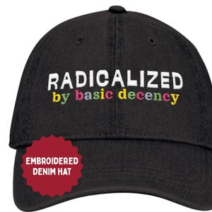 May include: Black denim hat featuring the embroidered phrase "RADICALIZED by basic decency" in white and multi-coloured text. The hat has a curved peak and a button on top. A red tag reads "EMBROIDERED DENIM HAT".
