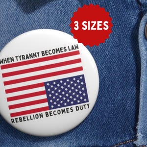 Könnte beinhalten: Ein weißer Knopf mit einem schwarz-roten amerikanischen Flaggenmuster. Die Flagge ist auf dem Kopf stehend. Der Text "When Tyranny Becomes Law Rebellion Becomes Duty" ist auf dem Knopf gedruckt.