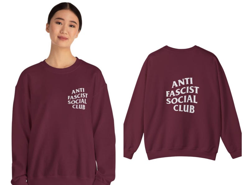 K&ouml;nnte beinhalten: Ein weinrotes Sweatshirt mit dem wei&szlig;en Text "ANTI FASCIST SOCIAL CLUB" auf der Vorder- und R&uuml;ckseite. Das Sweatshirt ist ein Rundhals-Modell und scheint aus einem weichen Material zu sein.