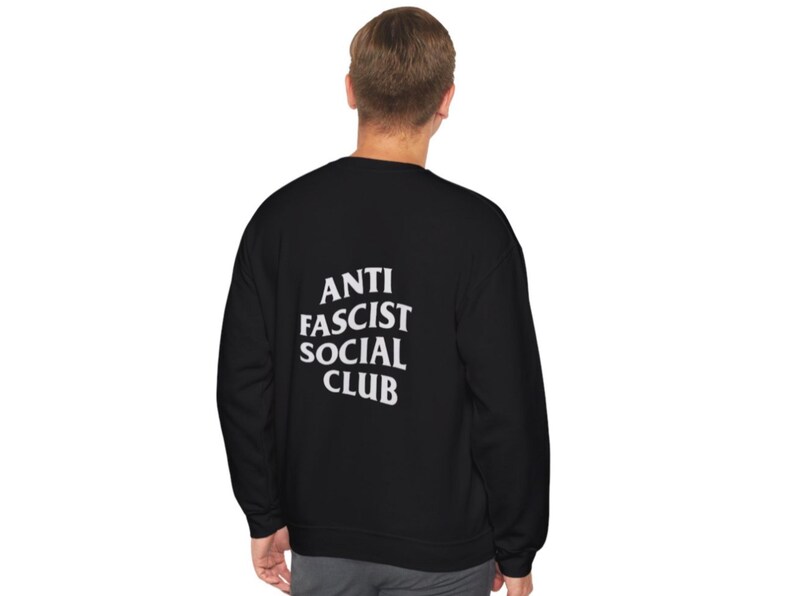 K&ouml;nnte beinhalten: Schwarzes Sweatshirt mit dem wei&szlig;en Text "ANTI FASCIST SOCIAL CLUB" auf dem R&uuml;cken. Das Sweatshirt ist einfarbig schwarz und scheint aus einem weichen Material zu sein.