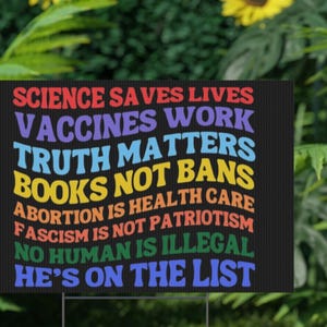 Op de afbeelding: Een zwart tuinbord met kleurrijke tekst. Het bord toont de zinnen: "Wetenschap redt levens, Vaccins werken, Waarheid doet ertoe, Geen boekenverboden, Abortus is gezondheidszorg, Fascisme is geen patriottisme, Geen mens is illegaal, Hij staat op de lijst."