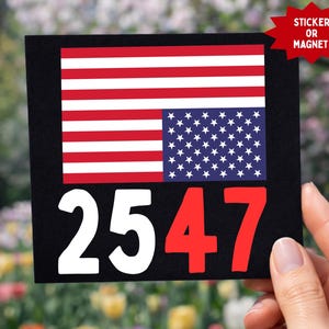 May include: Black square with the American flag design and the numbers "2547" in white and red. A red starburst sticker or magnet is in the upper right corner. The background is a blurred view of a garden.